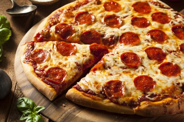 pepperoni pizza on a wooden board with one slice carved out but sitting by the pizza
